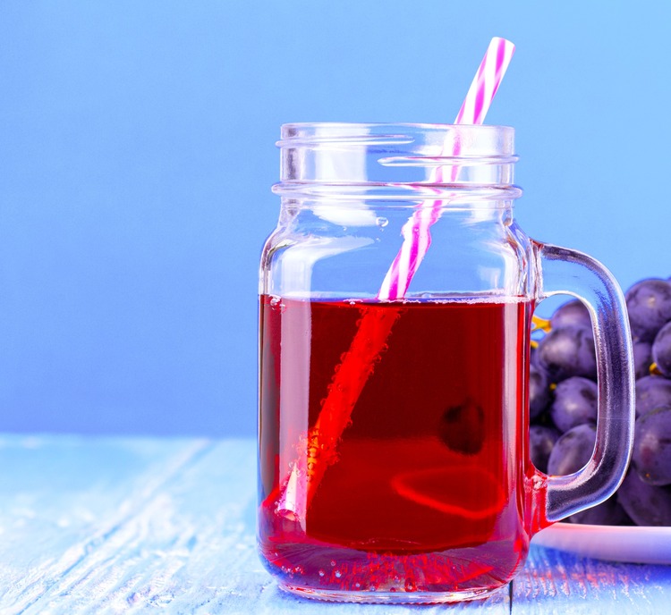 grape juice in a glass with a straw on a wooden table with a plate of grapes in the background