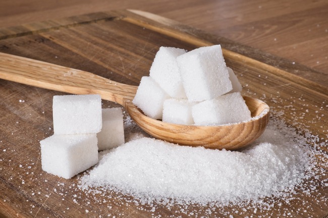 sugar cubes inside a wooden spoon with granulated sugar and more sugar cubes nearby