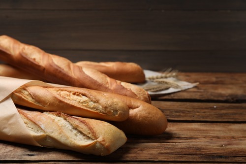 Freshly cooked baguettes wrapped in paper on a wooden table