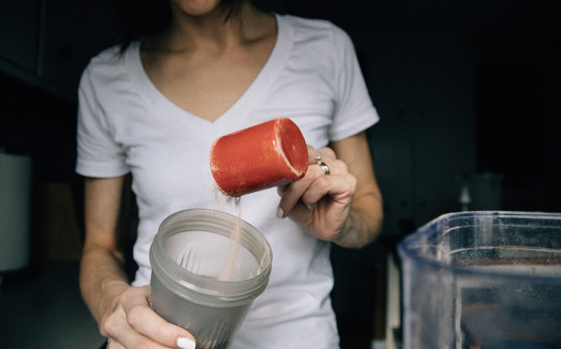 woman pouring protein powder into protein drink