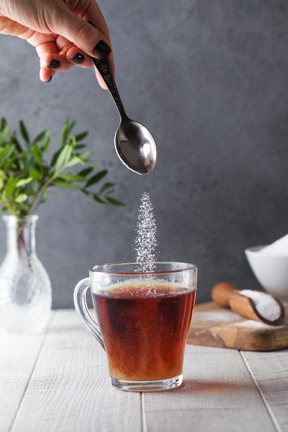 A spoon pouring erythritol into a cup of tea.