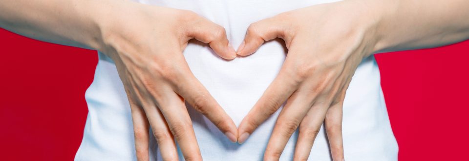 woman making the shape of a heart over her stomach