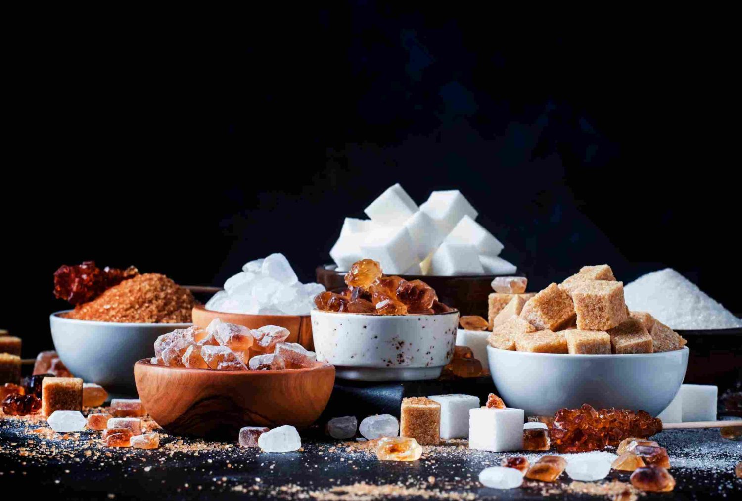 An assortment of different types of organic sugar in bowls on a table with a dark background
