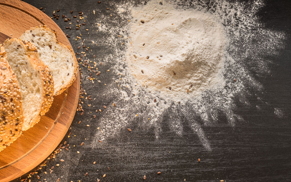 Bread with different seeds on a round wooden cutting board. Baking flour spilled on the table.