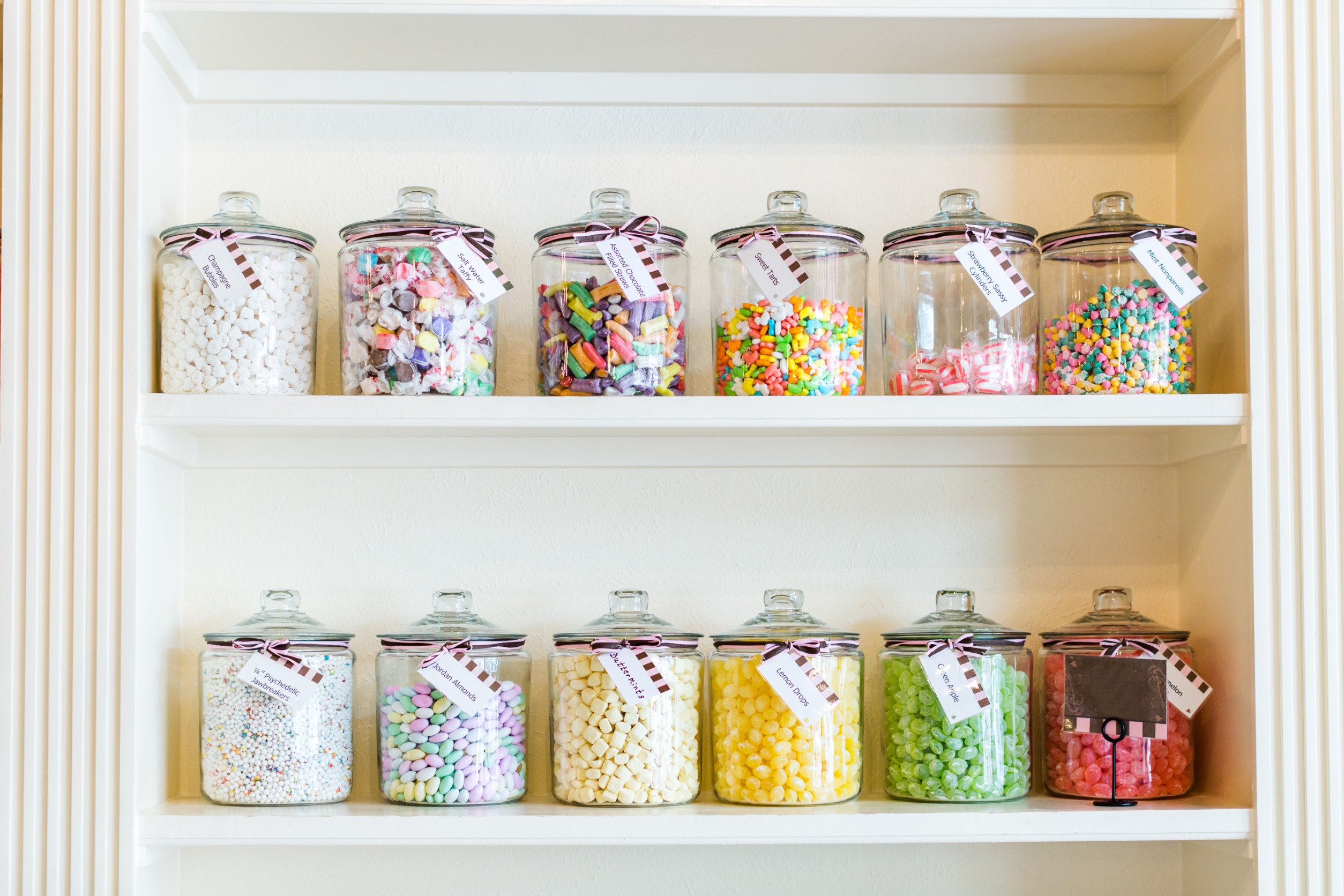 candy jars on a white shelf with tags