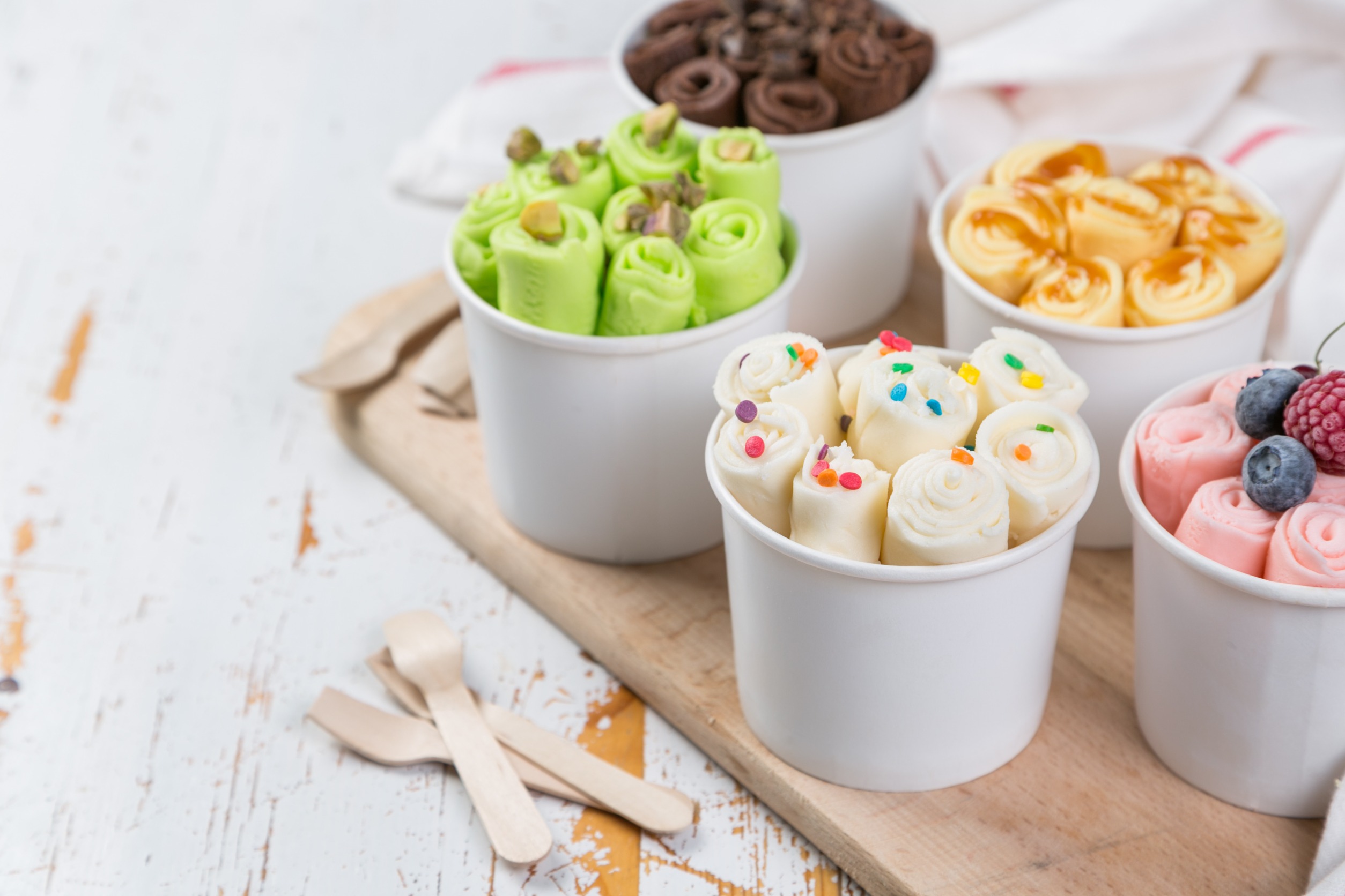 rolled ice cream bowls on a platter on a wooden table with wooden spoons