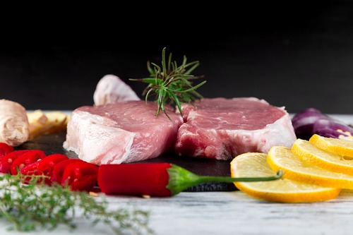 raw steak on a platter surrounded by herbs and vegetables