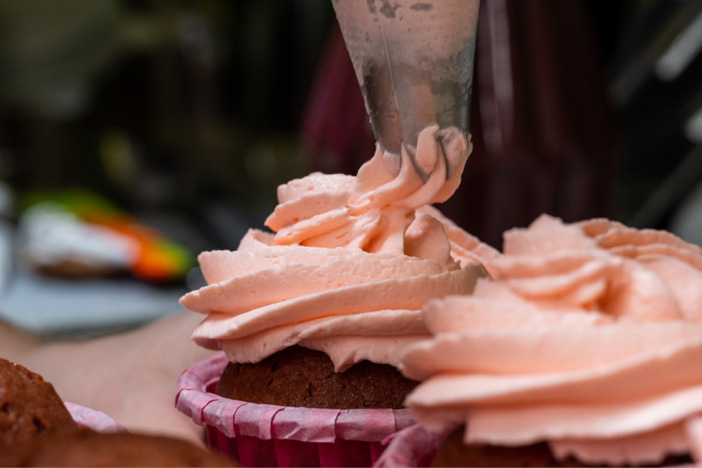 Chocolate cupcakes being decorated with a sweet pink frosting