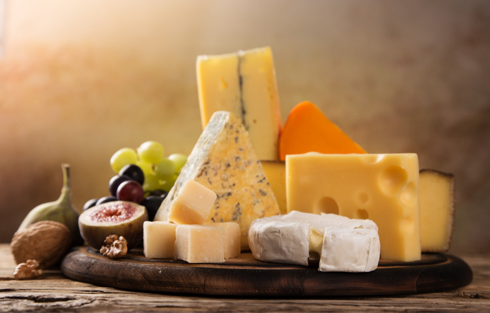 Various types of cheese and fruit on a round cutting board and wooden table