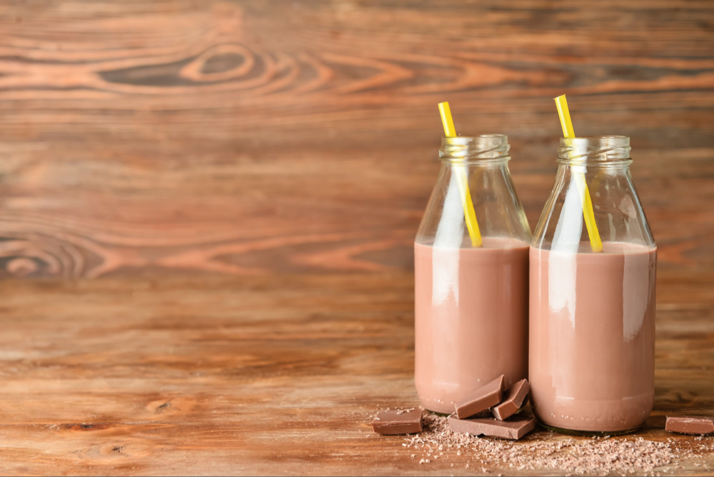 Chocolate milk in bottles on a wooden table with chocolate pieces and shavings from a dairy ingredient supplier
