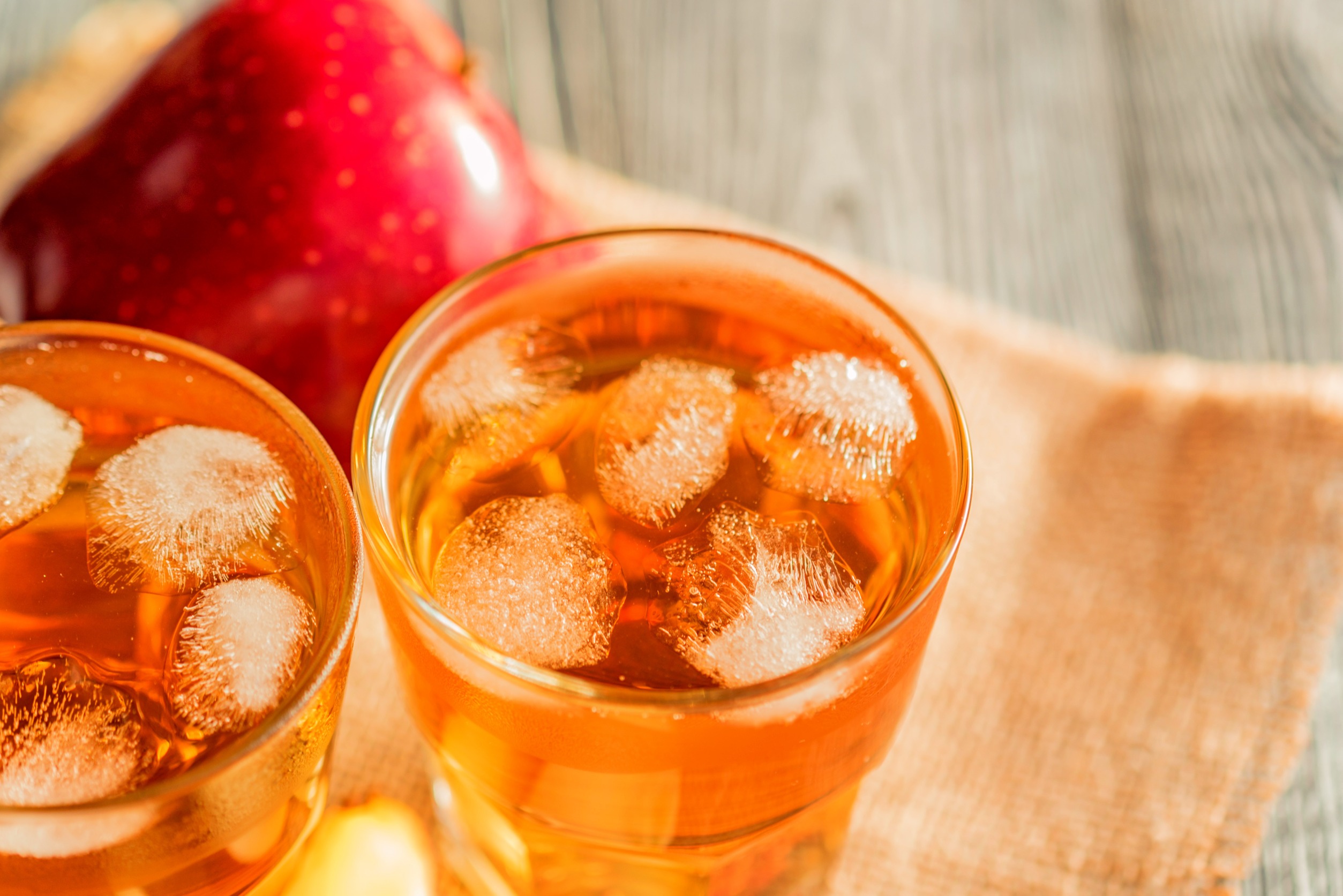 Two glasses of apple juice with ice and an apple in the background