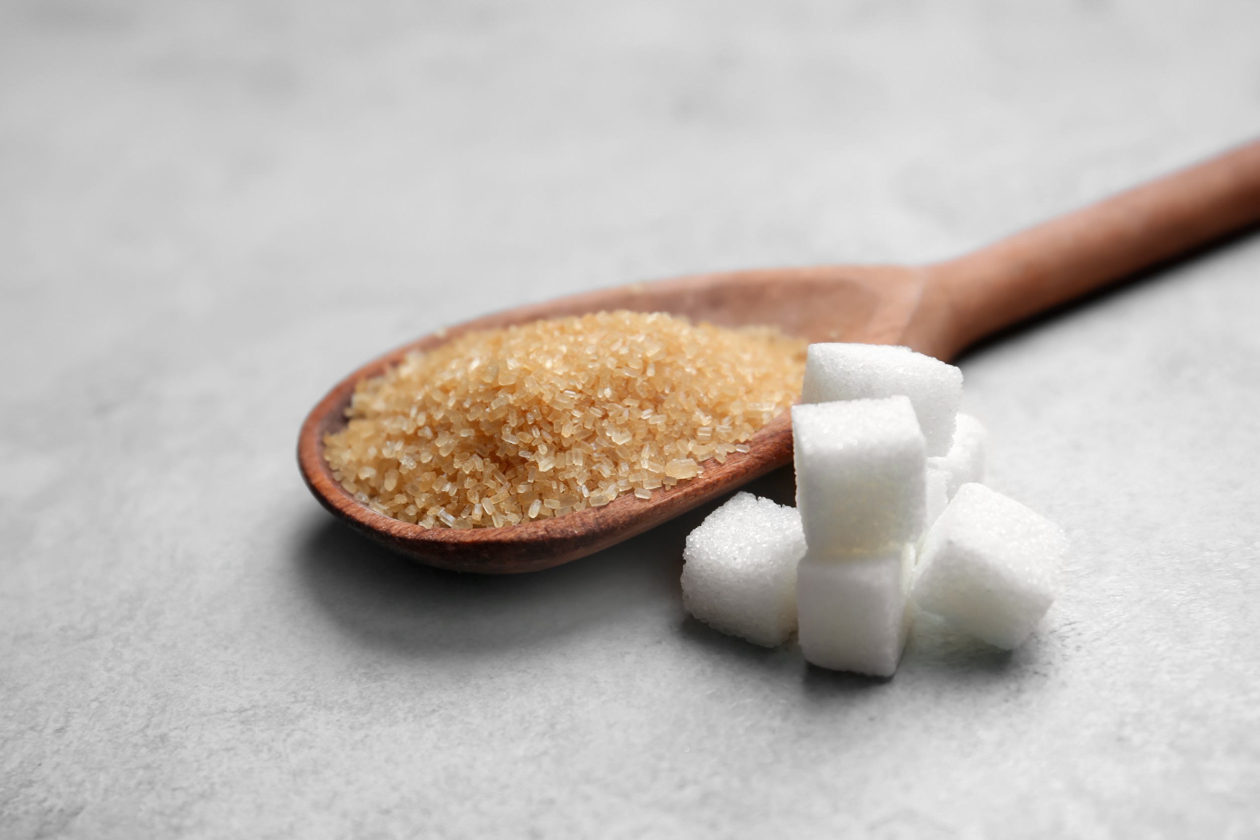 Organic sugar on a wooden spoon next to white sugar cubes