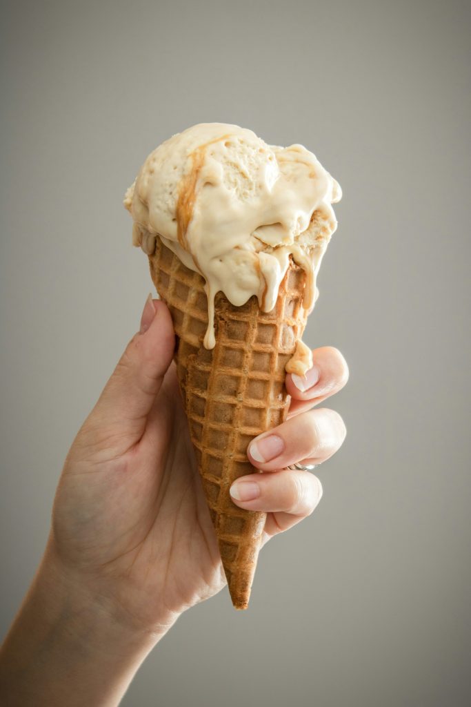 A hand holding an ice cream cone with vanilla and caramel ice cream