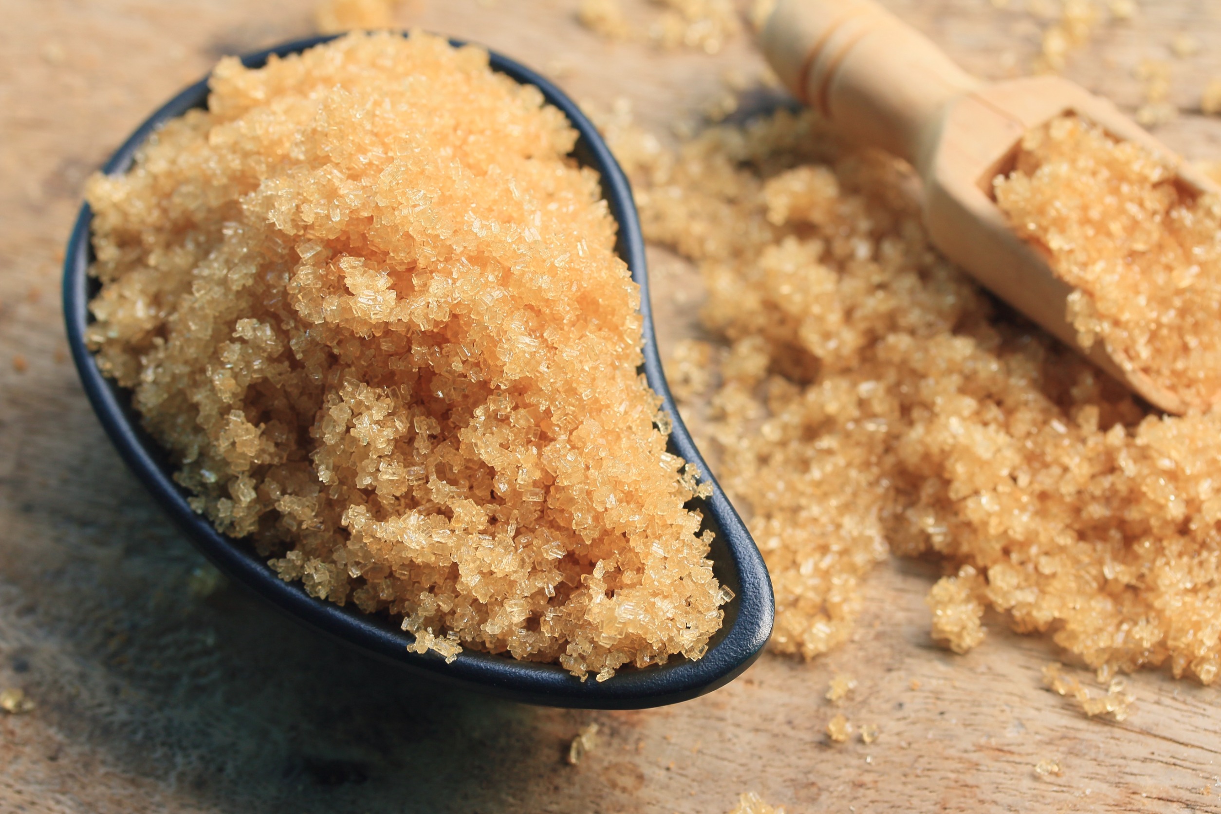 Brown organic cane sugar in a black bowl and a wooden spoon