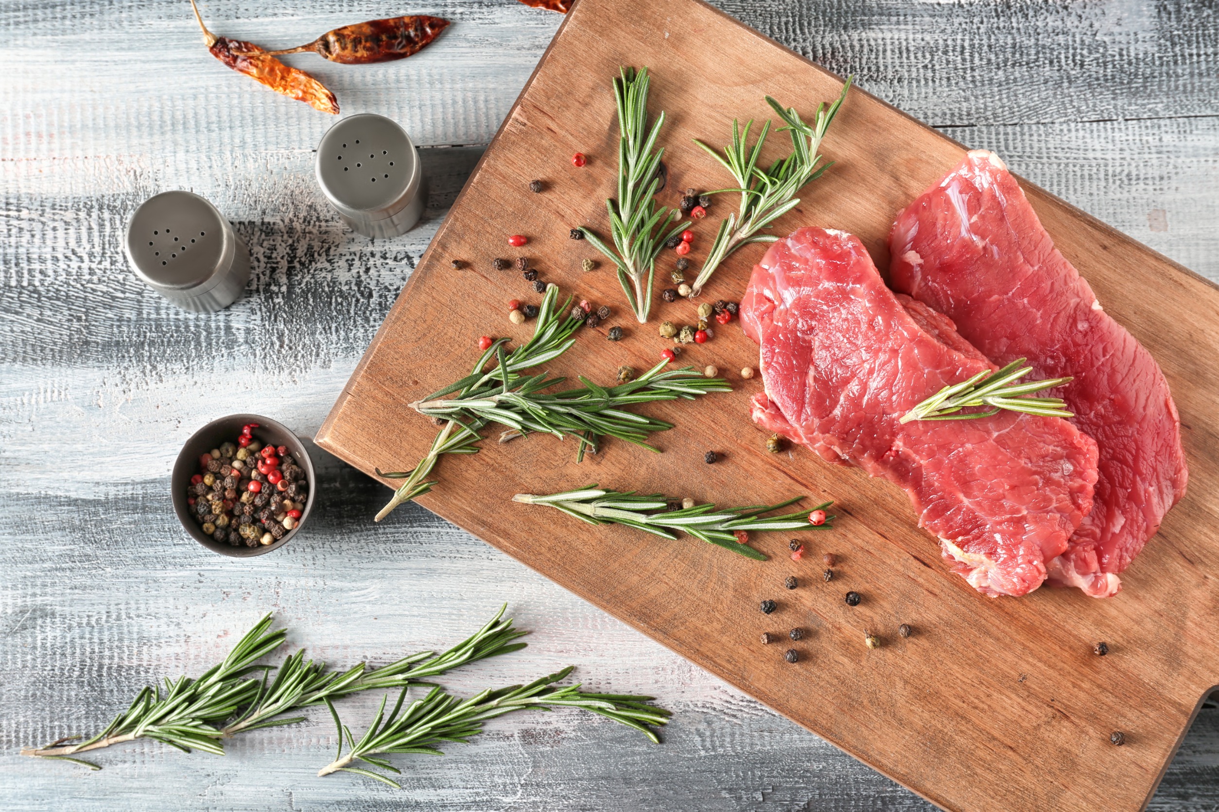 Raw meat on a cutting board with rosemary