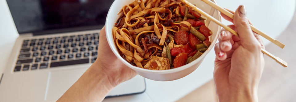 Ready-to-eat Asian noodle dish with laptop and office in the background