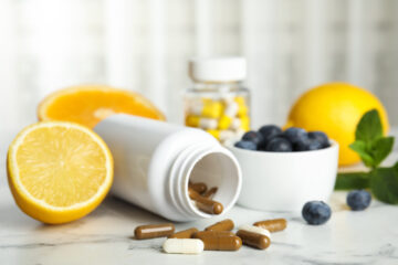 Bottle of vitamin pills accompanied by blueberries and lemon slices on a white marble table, highlighting functional ingredients for sports nutrition