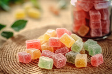 Assorted jelly candies in natural colors displayed on a woven mat beside a glass jar.