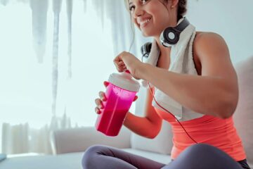 woman smiling and drinking a protein shake after a workout