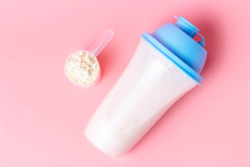 protein drink next to a scoop of protein powder on a pink background