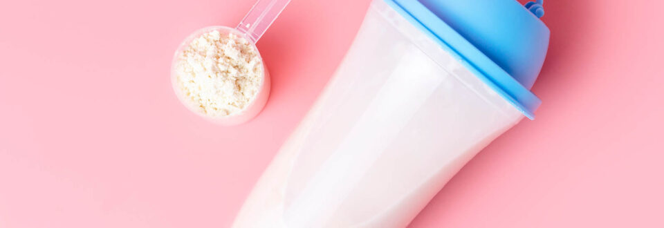 protein drink next to a scoop of protein powder on a pink background