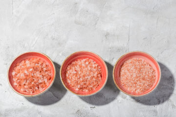 Three bowls on a table each filled with different sizes of pink himalayan salt
