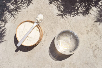 Plant-based protein powder and a glass of water on sand