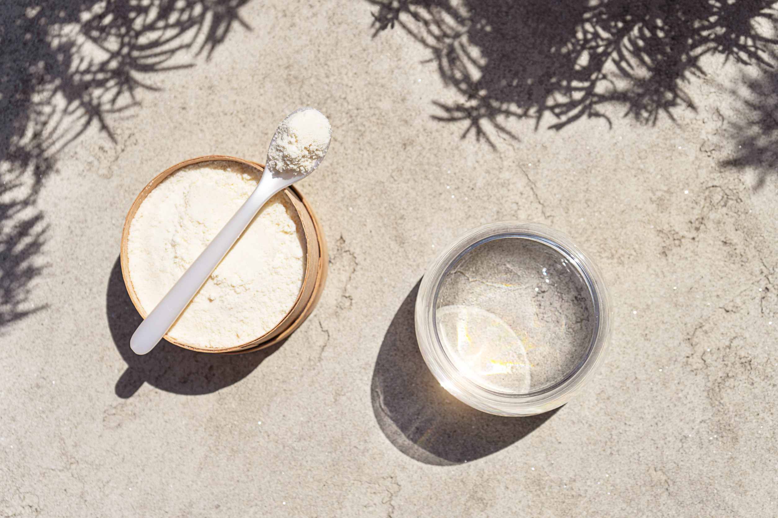 Plant-based protein powder and a glass of water on sand
